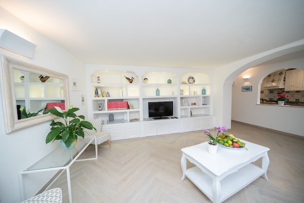 A modern living room with a TV, white furniture, and a plant on a table.