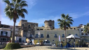 A coastal hotel with a tower, palm trees, and a sandy beach.