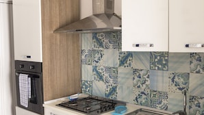 A modern kitchen with white cabinets, a black oven, a stainless steel range hood, and a tiled backsplash.