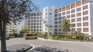 Et hotel med flere etager, altaner, parkeringsplads og grøn bevoksning omkring.