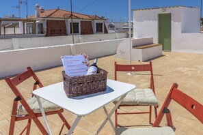 A rooftop terrace with a table and chairs, a wicker basket with a document, and a green door in the background.