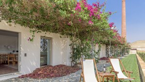 A garden with a white wall, a wooden table with chairs, and a tall brick chimney in the background. - FLH Cozy Tavira with Pool (Tavira)