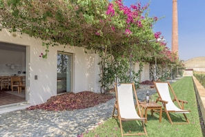 A garden with a white wall, a wooden table with chairs, and a tall brick chimney in the background. - FLH Cozy Tavira with Pool (Tavira)