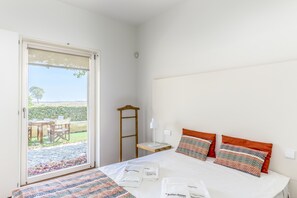 A bedroom with a bed, pillows, a bedside table, a lamp, and a view through a sliding door to an outdoor area with a table and chairs. - FLH Cozy Tavira with Pool (Tavira)