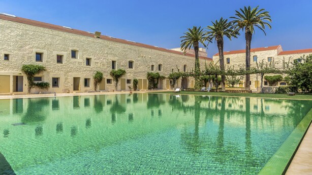 A pool area with clear water, a stone building with multiple windows, and palm trees. - FLH Cozy Tavira with Pool (Tavira)