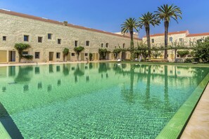 A pool area with clear water, a stone building with multiple windows, and palm trees. - FLH Cozy Tavira with Pool (Tavira)