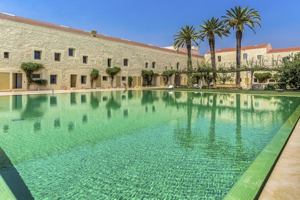 A pool area with clear water, a stone building with multiple windows, and palm trees. - FLH Cozy Tavira with Pool (Tavira)