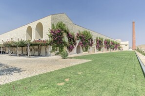 A building with arched windows and a brick facade, surrounded by a well-maintained lawn and flowering plants. - FLH Cozy Tavira with Pool (Tavira)
