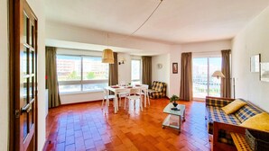 Een ruime woonkamer met een houten vloer, een eettafel met stoelen, een bank en een klein bijzettafeltje.