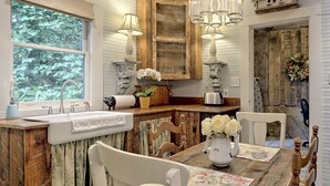Une cuisine rustique avec un îlot central en bois, des luminaires suspendus et une vue sur les arbres par une fenêtre.