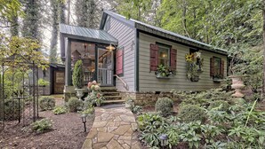 Un chalet rustique avec un sentier de pierres menant à l’entrée, entouré d’une végétation luxuriante et agrémenté de diverses plantes en pot.