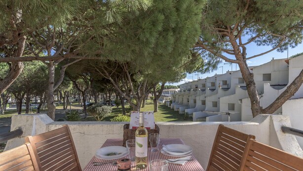 A table set for dining with a bottle of wine, glasses, and plates, overlooking a row of white buildings and trees. - FLH Albufeira Açoteias Apartment (Albufeira)