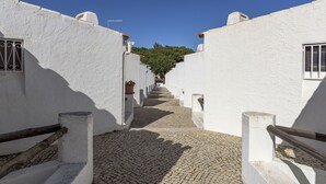 A narrow cobblestone street flanked by white buildings with barred windows and potted plants. - FLH Albufeira Açoteias Apartment (Albufeira)