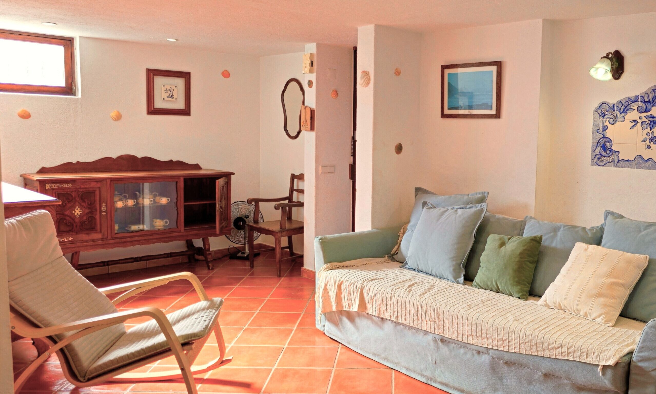 A living room with a wooden cabinet, a rocking chair, a sofa with cushions, and a tiled floor.