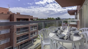 A balcony with a dining table set for four, surrounded by white chairs, overlooking a cityscape. - FLH Praia da Rocha Spacious Flat (Portimão)