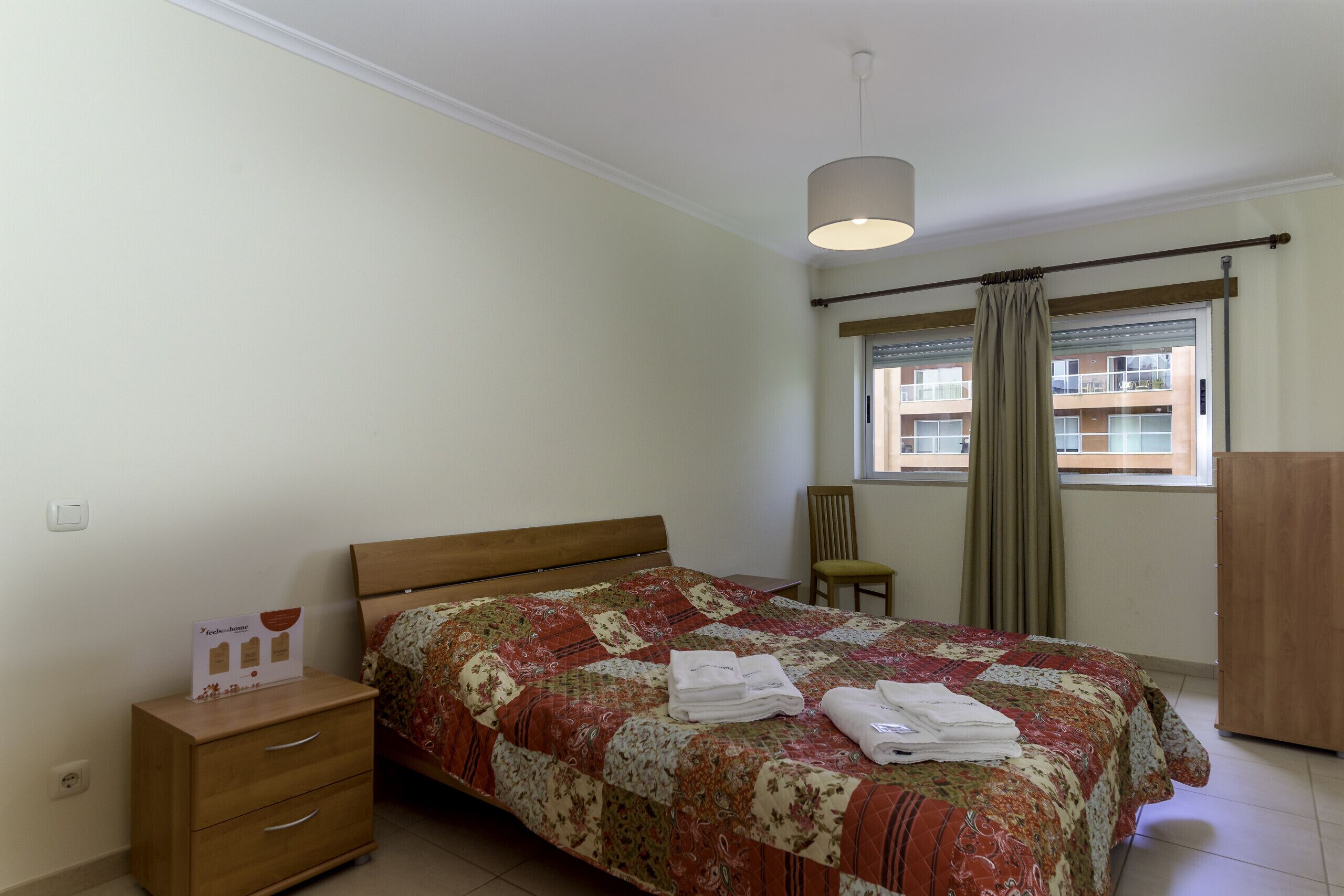 A bedroom with a bed, a nightstand, a chair, a wardrobe, and a window with curtains.