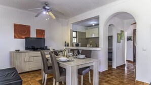 Cozinha moderna com área de refeições, com uma televisão de tela plana, mesa e cadeiras, e um ventilador de teto.