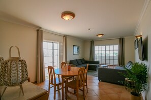 Een ruime woonkamer met een eettafel, stoelen, een bank en een groot raam.