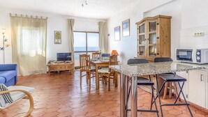 A spacious living area with a dining table, chairs, a sofa, and a TV. There is a kitchen area with a microwave and cabinets.