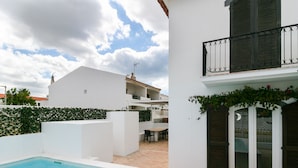 A swimming pool area with a white building, a balcony with dark shutters, and a patio with outdoor furniture. - FLH Altura Family House with Pool (Altura)