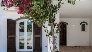 A building with white walls, two arched doorways, and a tree with pink flowers. - FLH Altura Family House with Pool (Altura)