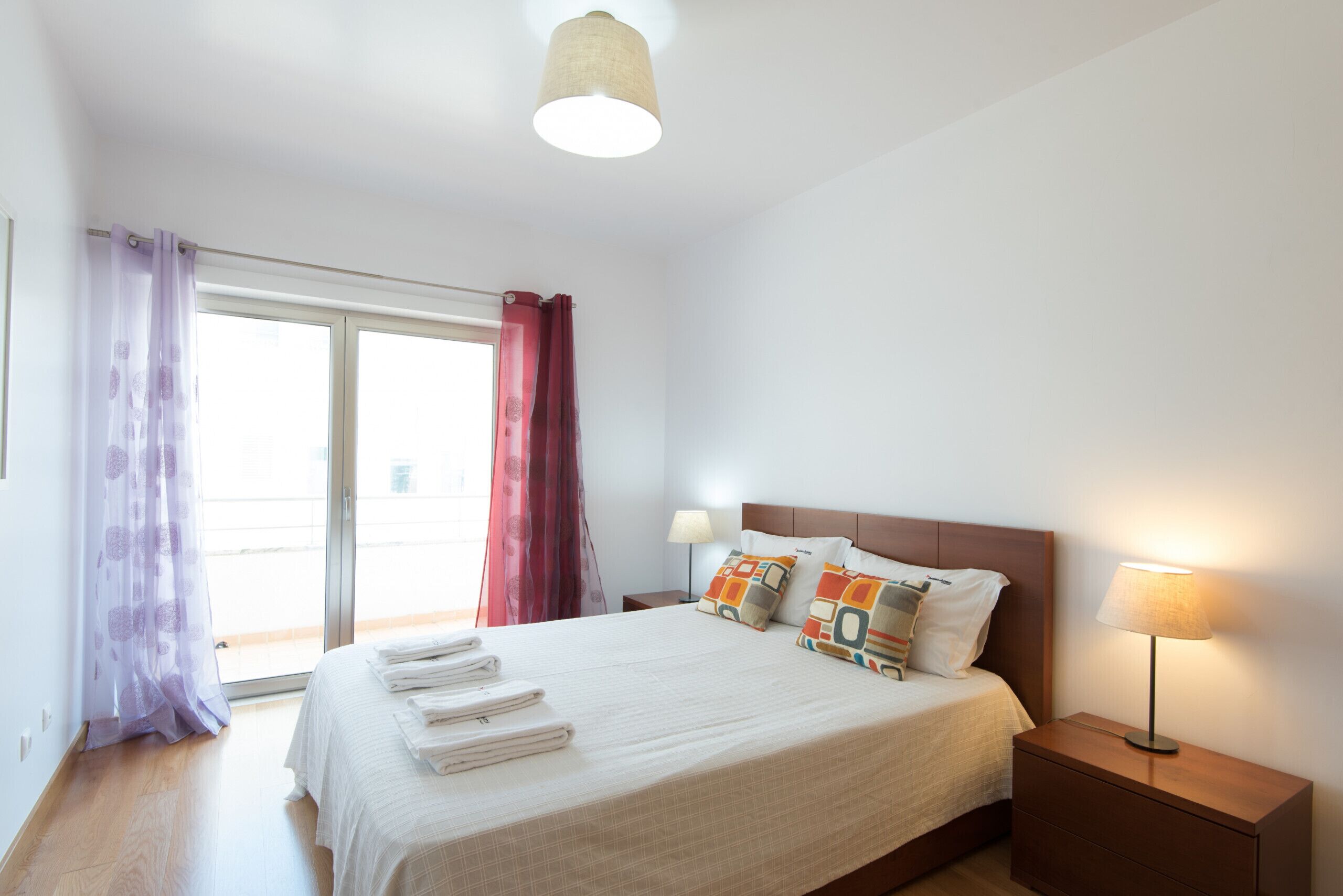 Ein Hotelzimmer mit Bett, Nachttisch, Lampe und Blick durch eine Schiebetür.