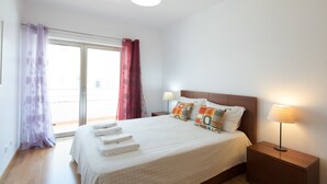 Ein Hotelzimmer mit Bett, Nachttisch, Lampe und Blick durch eine Schiebetür.