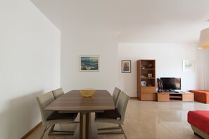A modern living room with a dining table, chairs, a TV, and a bookshelf.