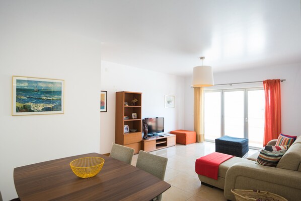 A modern living room with a dining table, sofa, and a television on a wooden stand.