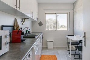 A compact kitchen with white cabinets, a stainless steel countertop, a red appliance, and a small window.