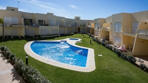 Um pátio com piscina, área de estar coberta e um edifício com várias varandas.