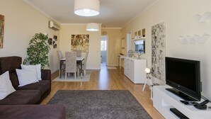 Uma sala de estar moderna com um sofá marrom, uma televisão e uma área de jantar com mesa e cadeiras.