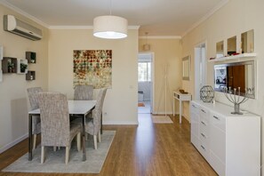 A modern dining area with a white table and grey upholstered chairs, a decorative mosaic wall, and a white cabinet with drawers.