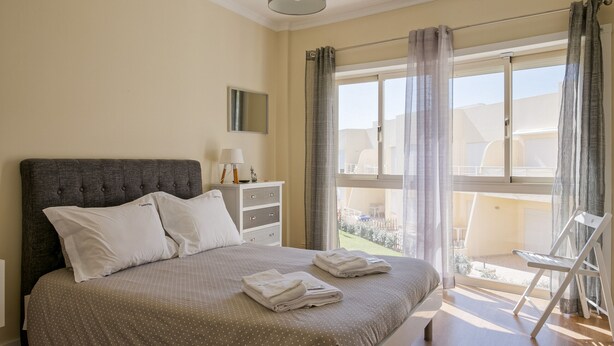 Quarto com cama grande, mesa de cabeceira, luminária e vista para o exterior.