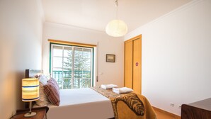 A bedroom with a bed, a bedside lamp, a window, and a door. - FLH Armação de Pêra Ocean View Flat (Armação de Pêra)
