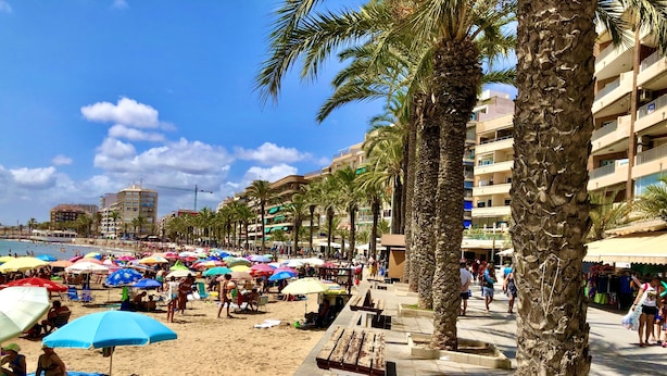 Een strand met palmbomen, parasols en mensen.