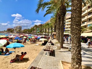 A beach with palm trees, umbrellas, and people.