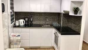 Een compacte keuken met witte kasten, een zwart aanrecht, een spoelbak en een fornuis.