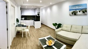 Een moderne woonkamer met een beige bank, een eettafel met stoelen, en een keuken op de achtergrond.