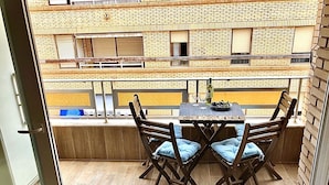 Een balkon met een houten tafel en stoelen, een fles wijn en een schaal fruit.