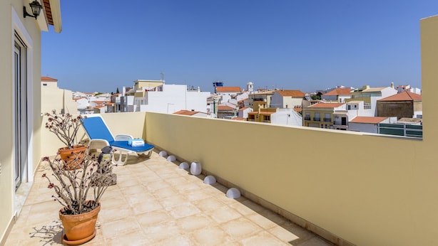 Un balcone con una pianta in vaso, una poltrona da relax blu e vista su una zona residenziale con diversi edifici.
