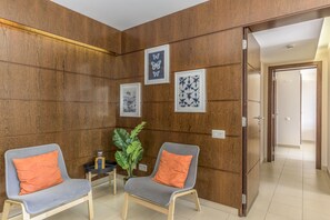 A room with two grey chairs with orange cushions, a small table with a plant, and framed artwork on the wall.