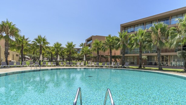 A swimming pool with clear blue water, surrounded by palm trees and lounge chairs. - FLH Salgados Beach Apartment (Albufeira)