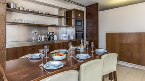 A modern dining area with a wooden table set for four, equipped with a built-in oven and microwave, and shelves above holding kitchenware. - FLH Salgados Beach Apartment (Albufeira)