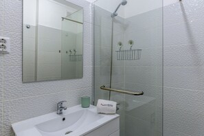 A bathroom with a white sink, a mirror, a shower with a glass door, and a towel rack. - FLH Vilamoura Cozy Flat with Balcony (Vilamoura)