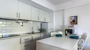 Une cuisine moderne avec des meubles blancs, un four encastré et un coin repas comprenant une table blanche et des assiettes bleues.