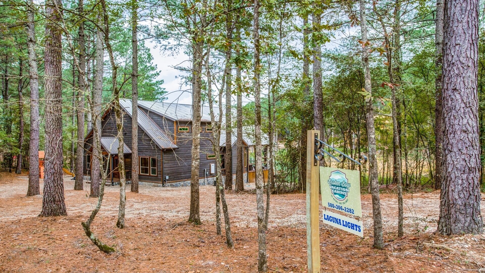 A cabin surrounded by tall trees with a sign indicating it is a vacation cabin.
