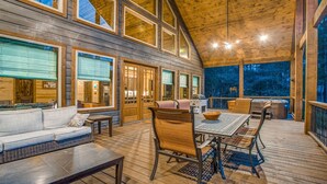A wooden deck with a dining table and chairs, a sofa, and a grill area. - Enjoy Pier on a Pond, Hot Tub, Playset, Games, Outdoor Furniture, Fireplace, TV (Broken Bow)