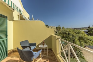 A balcony with two chairs and a small table, a bottle of wine, and a view of the surrounding landscape.