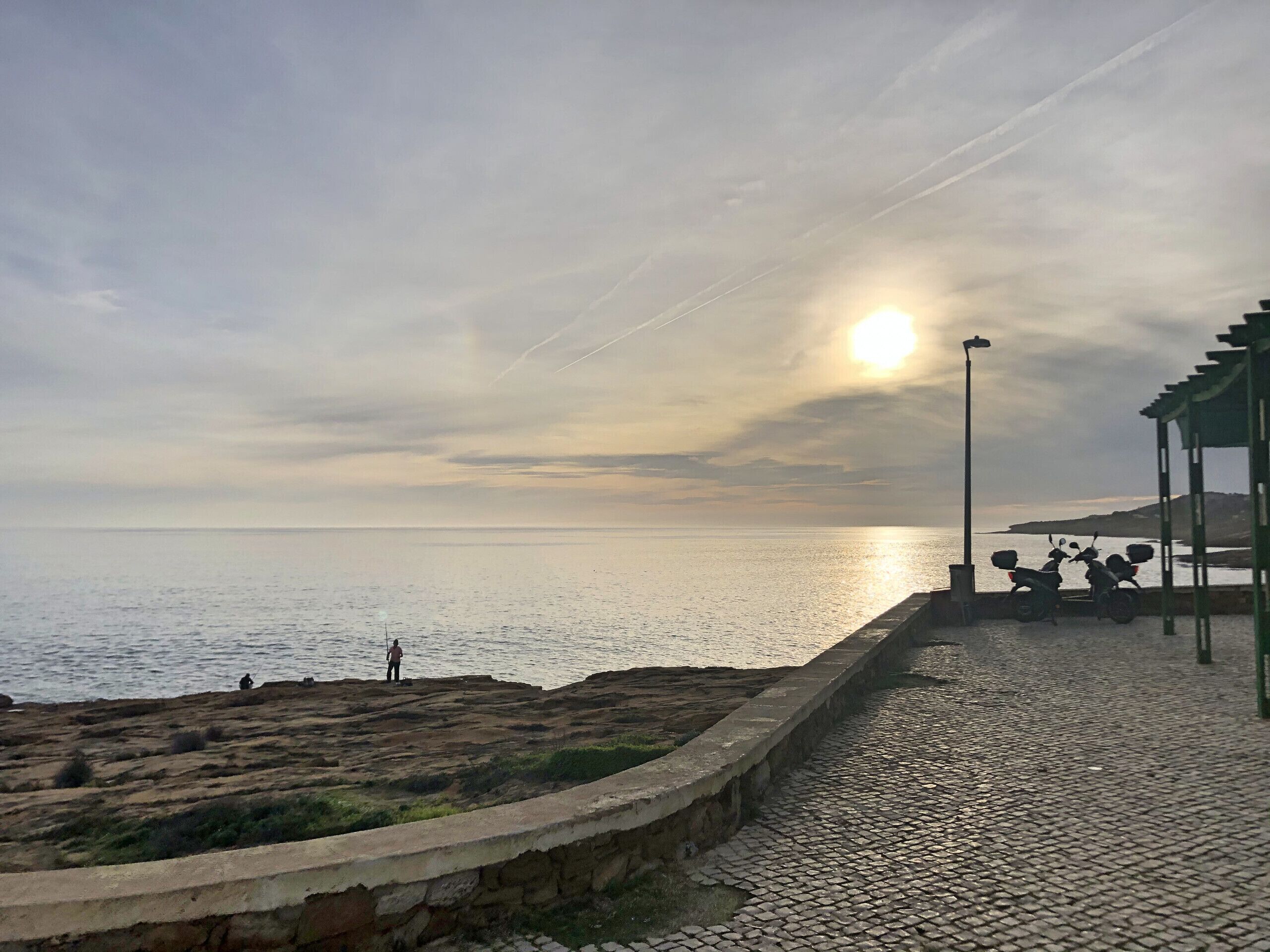 A coastal walkway with a stone pavement, a green structure, and a view of the sea.